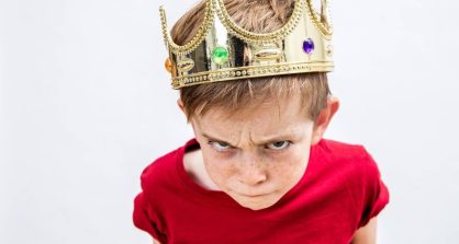 closeup of rebellious beautiful spoiled kid with frowning freckles wearing a king crown for mad attitude facing parenthood and education, white background, high angle view